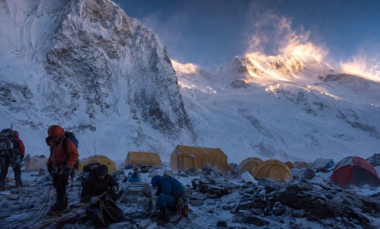 Mountaineers prepare beside tents at an advanced base camp beneath snow-covered Himalayan peaks.