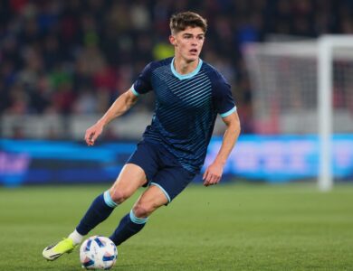 Professional footballer in a dark blue kit dribbling the ball during a stadium match