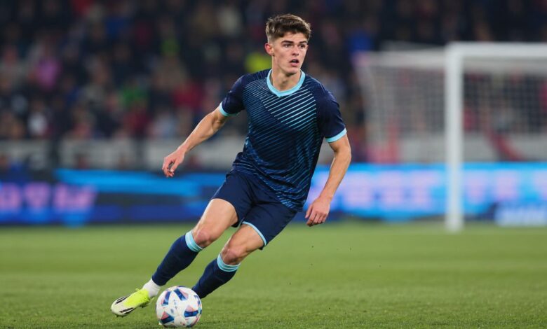 Professional footballer in a dark blue kit dribbling the ball during a stadium match