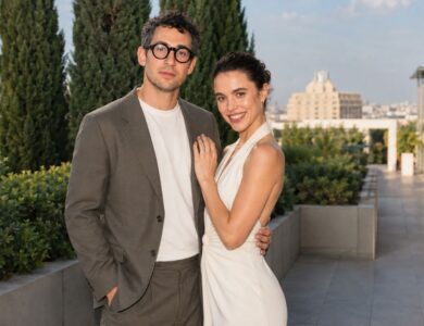 A stylish couple posing together on an outdoor terrace with greenery and city views in the background.