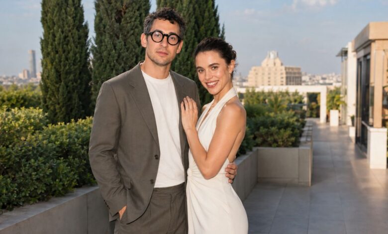 A stylish couple posing together on an outdoor terrace with greenery and city views in the background.