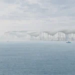 White cliffs of Dover across calm Channel waters at dawn with a distant boat on the water