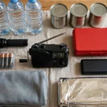 A household emergency kit with bottled water, tinned food, a torch, batteries, a wind-up radio and a first-aid kit on a table